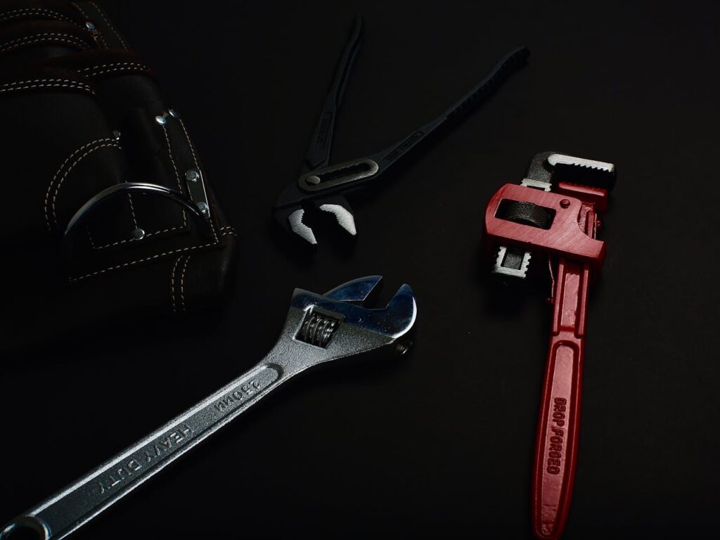 Close-up of various hand tools including wrenches and pliers on a dark surface.